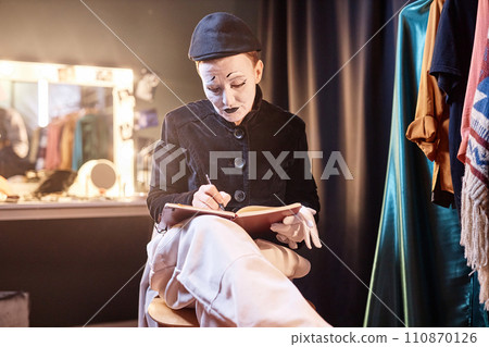 Dramatic portrait of mime performer preparing for show backstage and writing in notebook 110870126