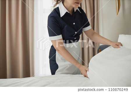 Close up of unrecognizable young maid adjusting pillows on hotel room bed with white sheets, copy space Close up of unrecognizable young maid adjusting pillows on hotel room bed with white sheets, copy space 110870249