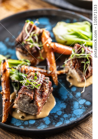 Three pieces of baked belly with grilled vegetables on a plate in a pub or restaurant Three pieces of baked belly with grilled vegetables on a plate in a pub or restaurant 110871333