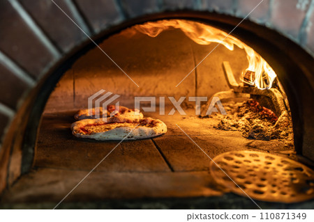 Traditional oven for baking pizza with burning wood and shovel. Several pizzas are baked in a brick oven 110871349