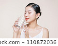 Young adult woman holds a glass of water in her hand near face 110872036