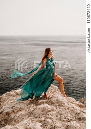 Woman sea green dress. Side view a happy woman with long hair in a long mint dress posing on a beach with calm sea bokeh lights on sunny day. Girl on the nature on blue sky background. 110872460