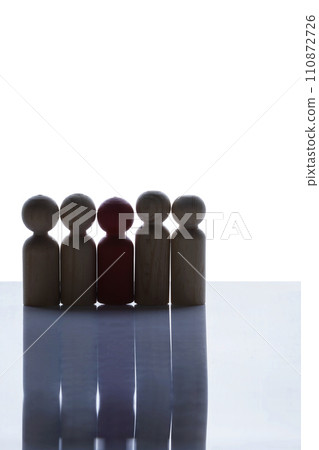 Closeup view of a red wooden figure standing on a row of brown wooden figures Closeup view of a red wooden figure standing on a row of brown wooden figures 110872726