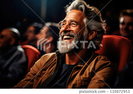 Happy gray haired elderly man laughs sitting in a cinema chair Happy gray haired elderly man laughs sitting in a cinema chair 110872953