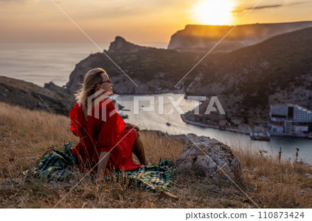 Woman sunset sea mountains. Happy woman siting with her back on the sunset in nature summer posing with mountains on sunset, silhouette. Woman in the mountains red dress, eco friendly, summer Woman sunset sea mountains. Happy woman siting with her back on the sunset in nature summer posing with mountains on sunset, silhouette. Woman in the mountains red dress, eco friendly, summer 110873424