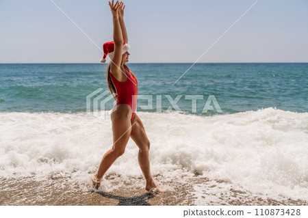 A woman in Santa hat on the seashore, dressed in a red swimsuit. New Year's celebration in a hot country. 110873428