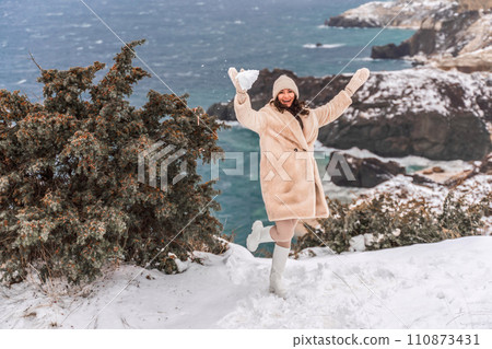 Woman snow sea. Amidst a wintry backdrop, a woman in a beige faux fur coat gleefully engages in a snowball fight, adding joy to the serene seascape. Woman snow sea. Amidst a wintry backdrop, a woman in a beige faux fur coat gleefully engages in a snowball fight, adding joy to the serene seascape. 110873431