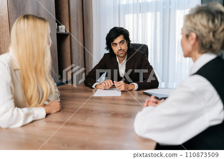 Front view of confident male mentor or corporate leader manager in suit communicate with business professional team, teaching staff group engaged in discussion at training meeting sitting at table. Front view of confident male mentor or corporate leader manager in suit communicate with business professional team, teaching staff group engaged in discussion at training meeting sitting at table. 110873509