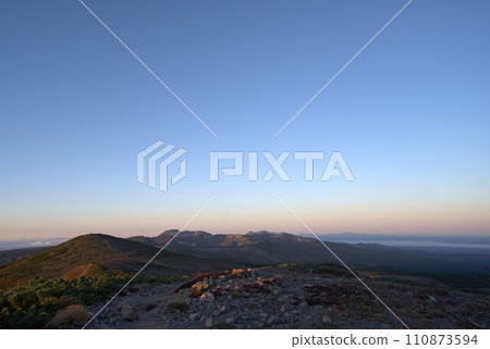The mountain trail illuminated by the morning sun, Mt. Tomuraushi in the distance 110873594