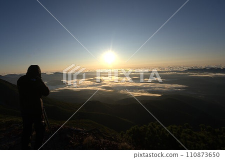 Photographer taking pictures of the sunrise from the mountaintop 110873650