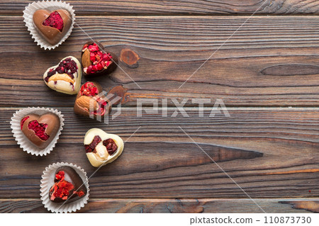 chocolate sweets in the form of a heart with fruits and nuts on a colored background. top view with space for text, holiday concept chocolate sweets in the form of a heart with fruits and nuts on a colored background. top view with space for text, holiday concept 110873730