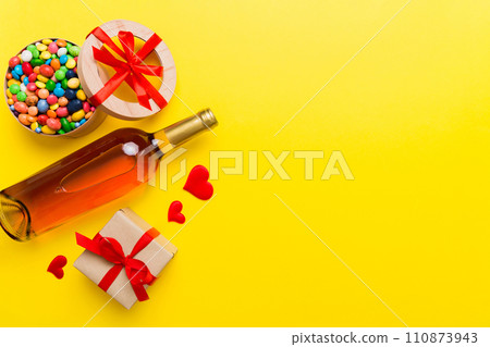 Bottle of red wine on colored background for Valentine Day with gift and chocolate. Heart shaped with gift box of chocolates top view with copy space 110873943