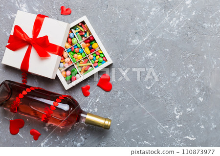 Bottle of red wine on colored background for Valentine Day with gift and chocolate. Heart shaped with gift box of chocolates top view with copy space 110873977