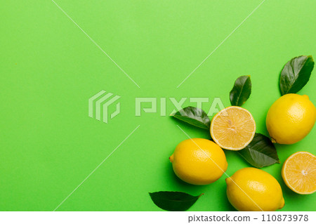 Many fresh ripe lemons with green leaves on colored background, top view, space for text 110873978