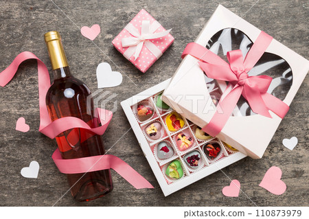 Bottle of red wine on colored background for Valentine Day with gift and chocolate. Heart shaped with gift box of chocolates top view with copy space 110873979