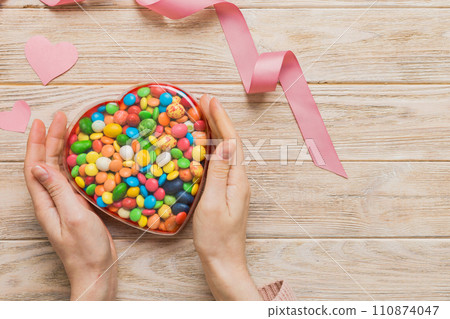 Female hands with delicious candies in box on color background Female hands with delicious candies in box on color background 110874047