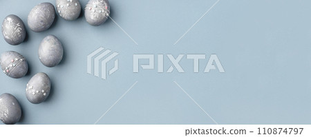 Festive Easter background. Gray-blue Easter eggs with stars on a blue table. Banner with a place for text. Top view. 110874797