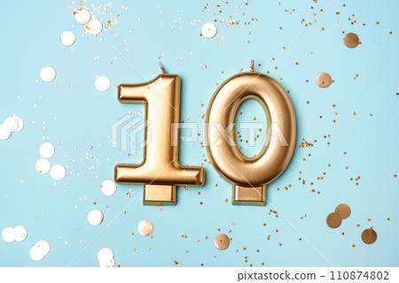 Gold candle in the form of number ten on blue background with confetti. Gold candle in the form of number ten on blue background with confetti. 110874802