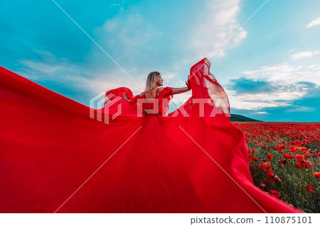 Woman poppy field red dress. Happy woman in a long red dress in a beautiful large poppy field. Blond stands with her back posing on a large field of red poppies 110875101
