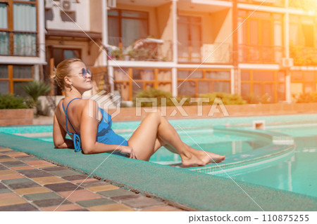 Bikini-clad woman enjoys poolside relaxation. Poolside ambiance. Capturing woman's relaxed time near pool. Bikini-clad woman enjoys poolside relaxation. Poolside ambiance. Capturing woman's relaxed time near pool. 110875255