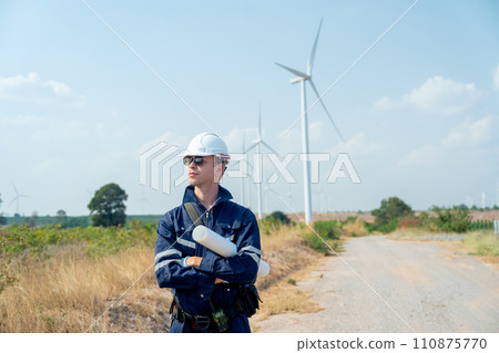 Professional technician worker man stand with arm-crossed and stand with look to his right side in front of wind turbine or windmill in the field and in concept of green energy for good environment. 110875770