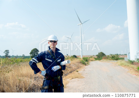 Professional technician worker man stand with hold plan paper and look forward in front of wind turbine or windmill with blue sky in concept of green energy for good environment. Professional technician worker man stand with hold plan paper and look forward in front of wind turbine or windmill with blue sky in concept of green energy for good environment. 110875771