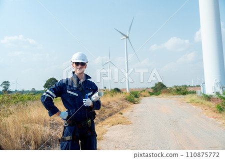 Professional technician worker man with smiling and stand with look at camera in front of wind turbine or windmill with blue sky in concept of green energy for good environment. 110875772