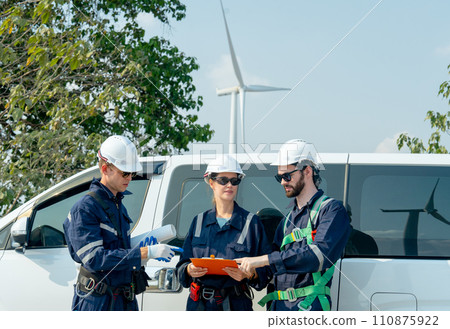 Group of technician workers stand beside the van and discuss about work with windmill or wind turbine on the background. Group of technician workers stand beside the van and discuss about work with windmill or wind turbine on the background. 110875922