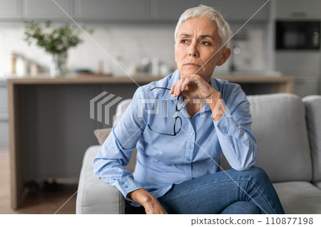 European mature woman feels unhappy touching chin in living room European mature woman feels unhappy touching chin in living room 110877198