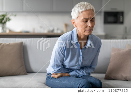 Unhappy Senior Woman Having Stomachache Sitting On Sofa At Home Unhappy Senior Woman Having Stomachache Sitting On Sofa At Home 110877215