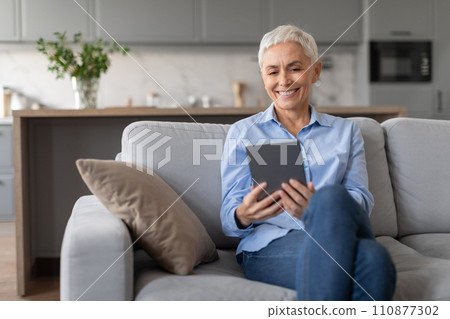 Happy senior woman sitting with digital tablet at living room 110877302