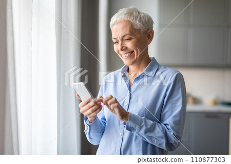 Smiling Senior Lady Using Mobile Phone Texting Standing At Home 110877303