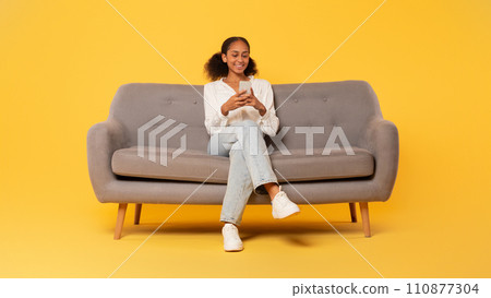 African american student teenager girl using smartphone on couch, studio African american student teenager girl using smartphone on couch, studio 110877304