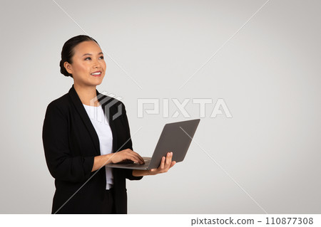 Asian businesswoman in a black blazer with a content smile working on a laptop 110877308