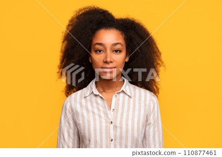 Serene black woman with curly hair in striped shirt on yellow background Serene black woman with curly hair in striped shirt on yellow background 110877461