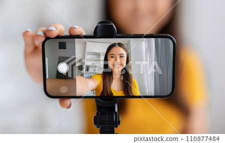 Smiling asian female vlogger creating content, using a smartphone mounted on tripod Smiling asian female vlogger creating content, using a smartphone mounted on tripod 110877484