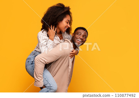 Black man giving piggyback ride to woman on yellow background 110877492