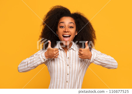 Cheerful black woman giving two thumbs up against yellow wall Cheerful black woman giving two thumbs up against yellow wall 110877525