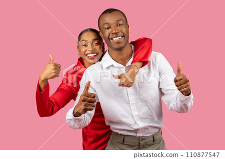 Happy black couple giving thumbs up, woman in red, man in white, pink background Happy black couple giving thumbs up, woman in red, man in white, pink background 110877547