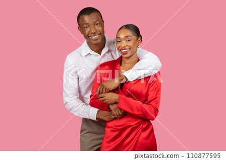 Affectionate black couple posing, man in white, woman in red, pink backdrop 110877595