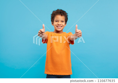 Happy boy giving thumbs up in orange t-shirt, blue background 110877635