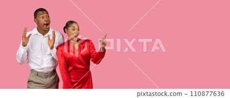 Excited black couple pointing and reacting, pink background, panorama with free space 110877636
