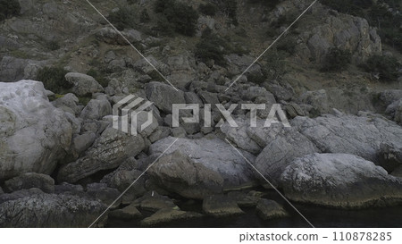 The coast of the bay in the White Sea Close-up view of large white and grey stones near the mountain slope and small stream or mountain river. Shot. Rocky side of a cliff near water 110878285