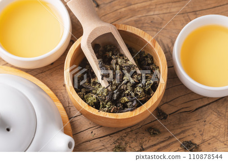 Tea leaves in wood bowl closeup with scoop and tea set on wooden table 110878544