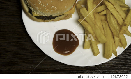 French fries with ketchup and hamburger. Cheeseburger with french fries on a white plate. Delicious fast food French fries with ketchup and hamburger. Cheeseburger with french fries on a white plate. Delicious fast food 110878632