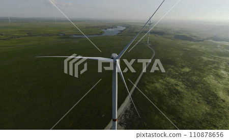 Flying at wind generators. Shot. Beautiful landscape with wind power generators on green fields. Windmills generate energy from the wind in fields. Wind energy Flying at wind generators. Shot. Beautiful landscape with wind power generators on green fields. Windmills generate energy from the wind in fields. Wind energy 110878656