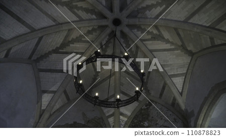 View from the bottom on the old chandelier in the form of a wheel with light bulbs hanging on the ceiling in church or another old building. Action. Beautiful retro style View from the bottom on the old chandelier in the form of a wheel with light bulbs hanging on the ceiling in church or another old building. Action. Beautiful retro style 110878823