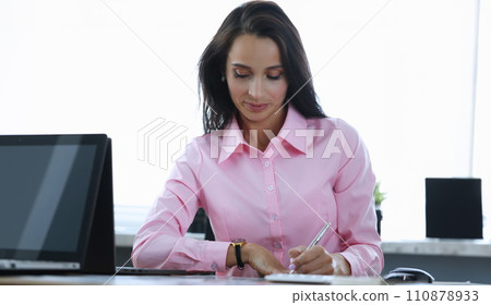 Girl makes notes with pen, at table in office 110878933