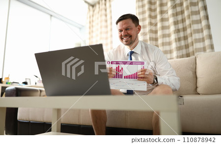 Guy is sitting at home in front laptop with report 110878942