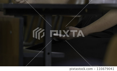 Woman hand using a smart phone under a wooden table. Woman uses the Internet on your phone during the exam Woman hand using a smart phone under a wooden table. Woman uses the Internet on your phone during the exam 110879041
